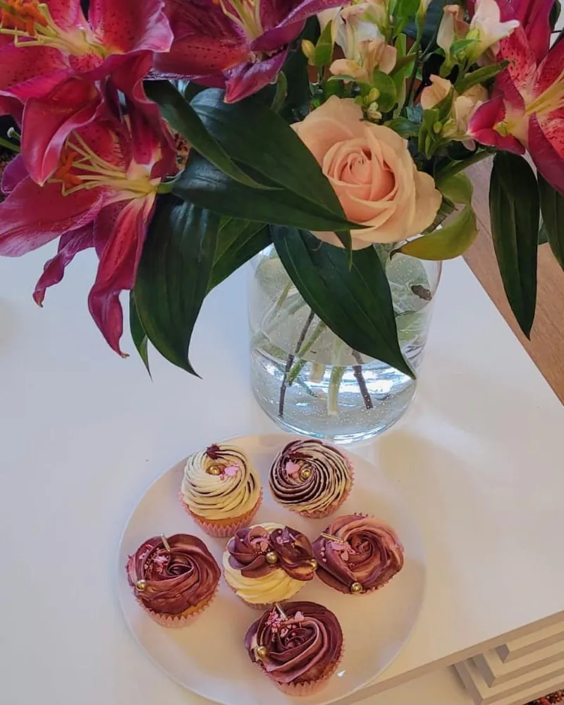 Burgundy and cream rose-piped cupcakes with gold pearls beside a vase of pink lilies