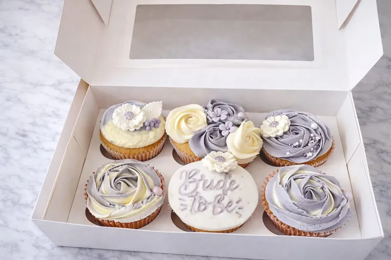 Lilac and cream rose cupcakes with sugar daisies and a Bride to Be disc in a gift box