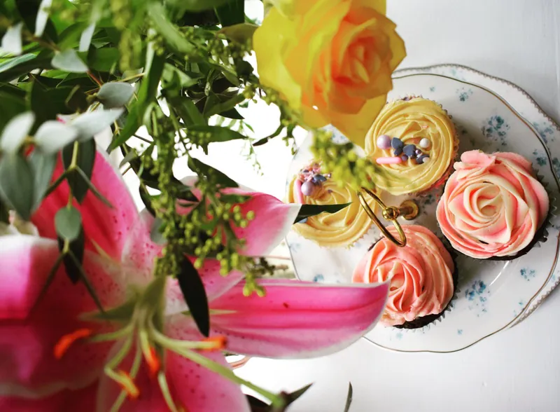 Pink and lemon rose cupcakes on a floral plate with a yellow rose and pink lily