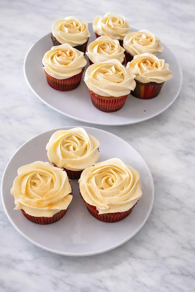 Ivory rose-piped cupcakes with a light gold dusting on two white plates